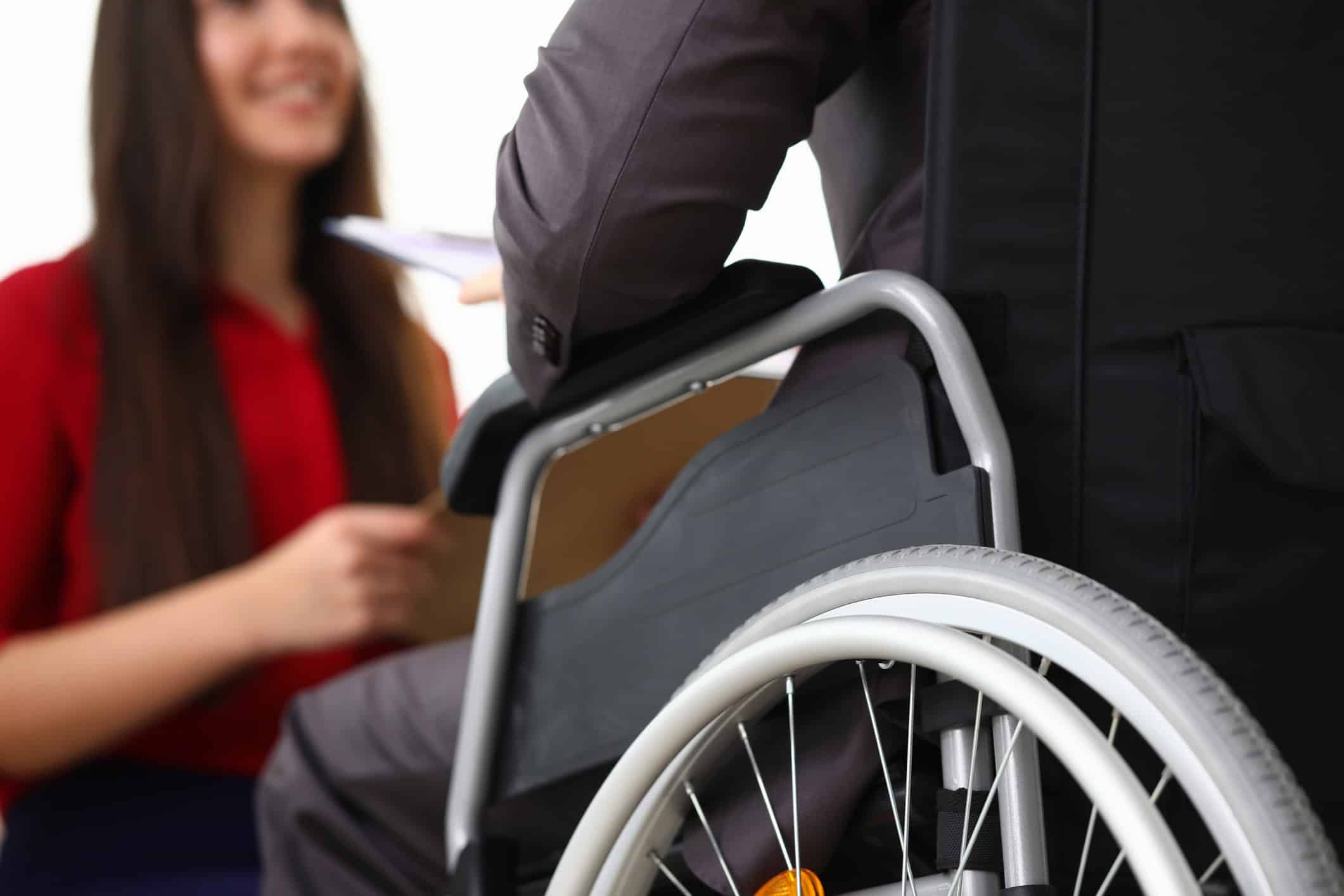 A person in a wheelchair interacting with a smiling woman in a red shirt, symbolizing a positive and inclusive workplace environment.