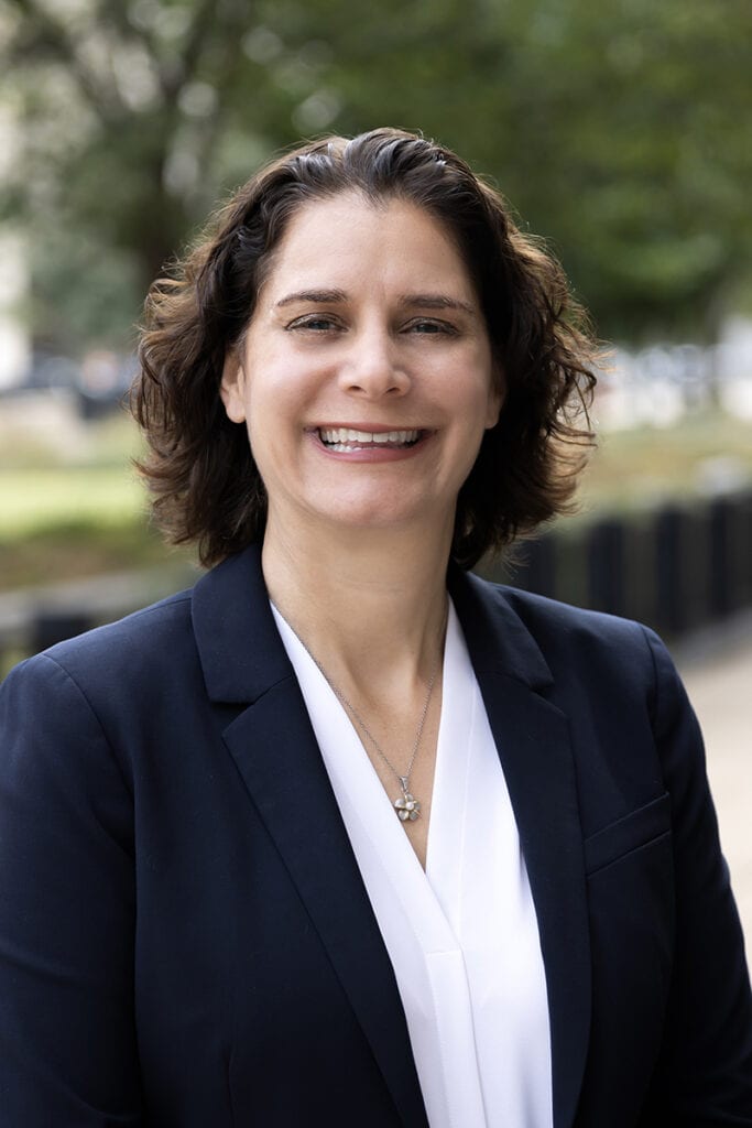 A professional headshot of Alison Barkoff smiling while wearing a navy blue blazer and white blouse.