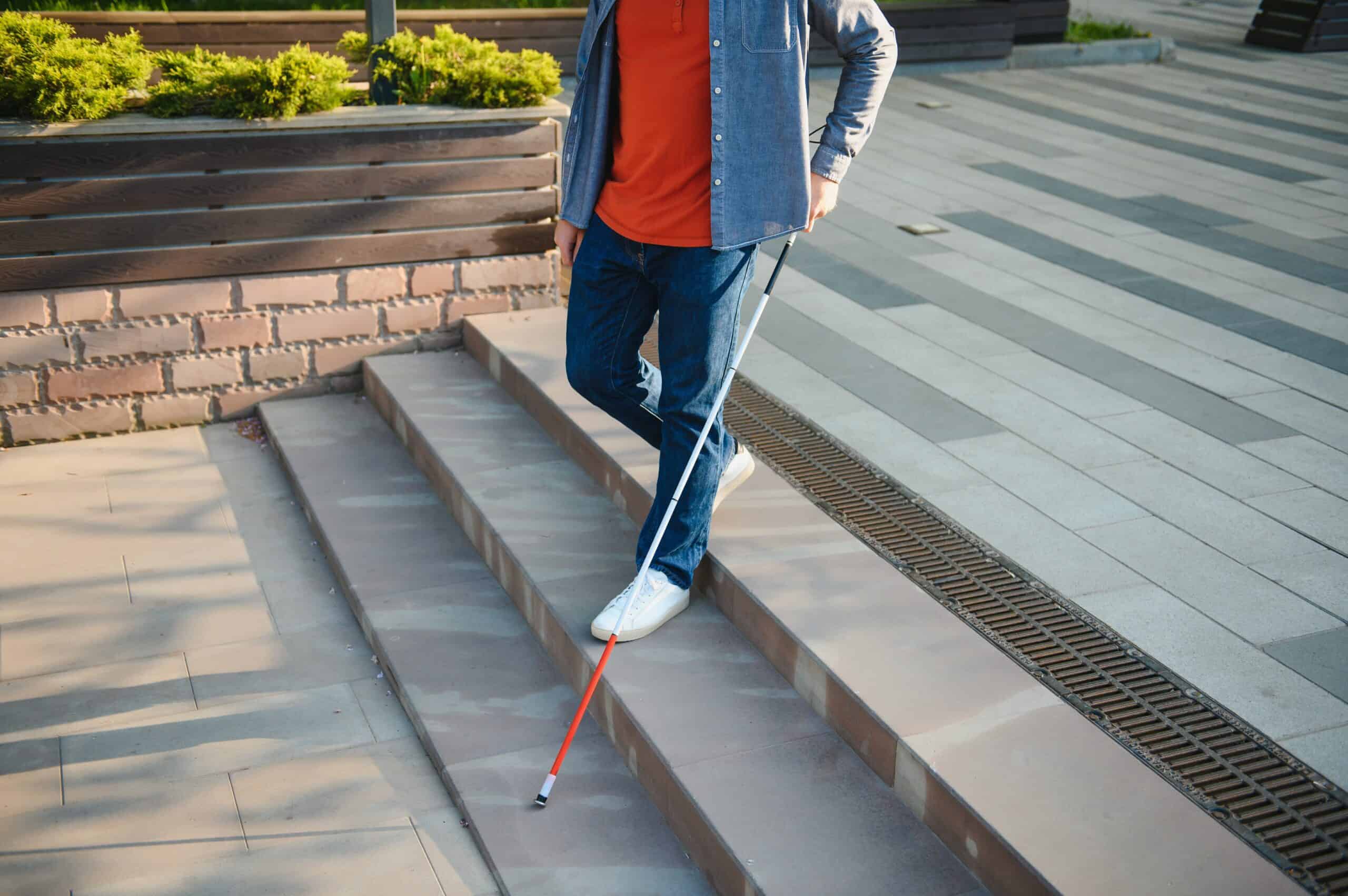 In a city, a blind traveler independently navigates an outdoor plaza, using their cane as they walk down some stairs.