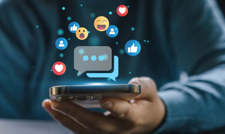 A person holding a smartphone with various emojis floating above it.