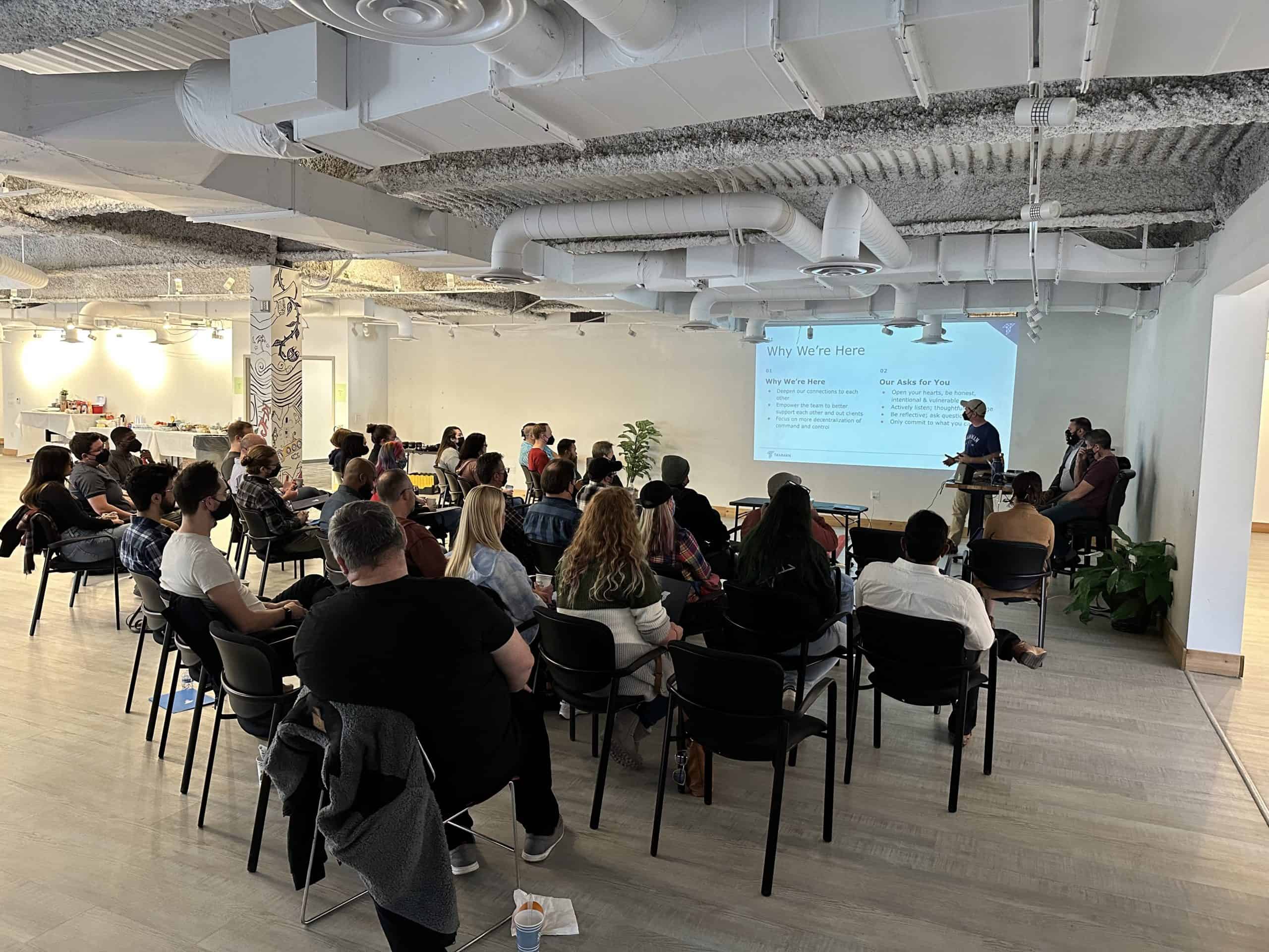A large group of Tamman employees gather around for a presentation.