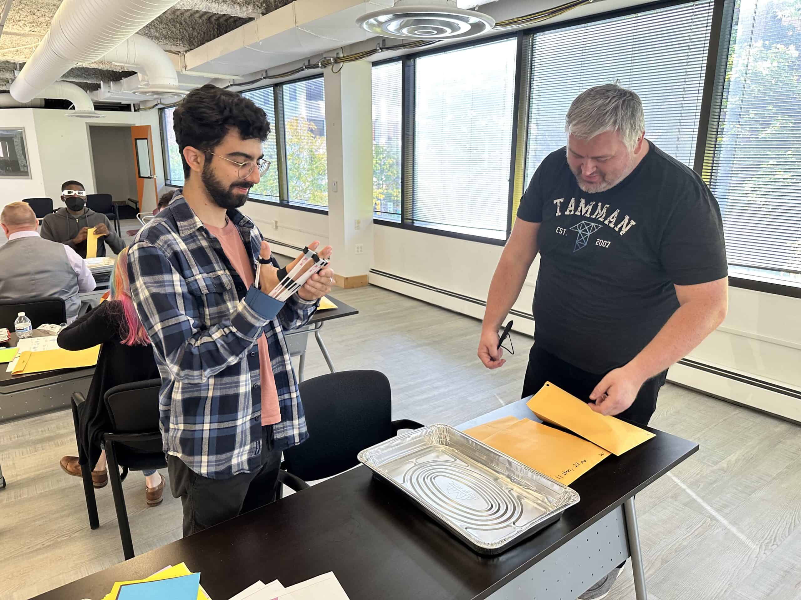 Devon and Bill prepare to build a small Lego set while wearing gloves that simulate severe arthritis.