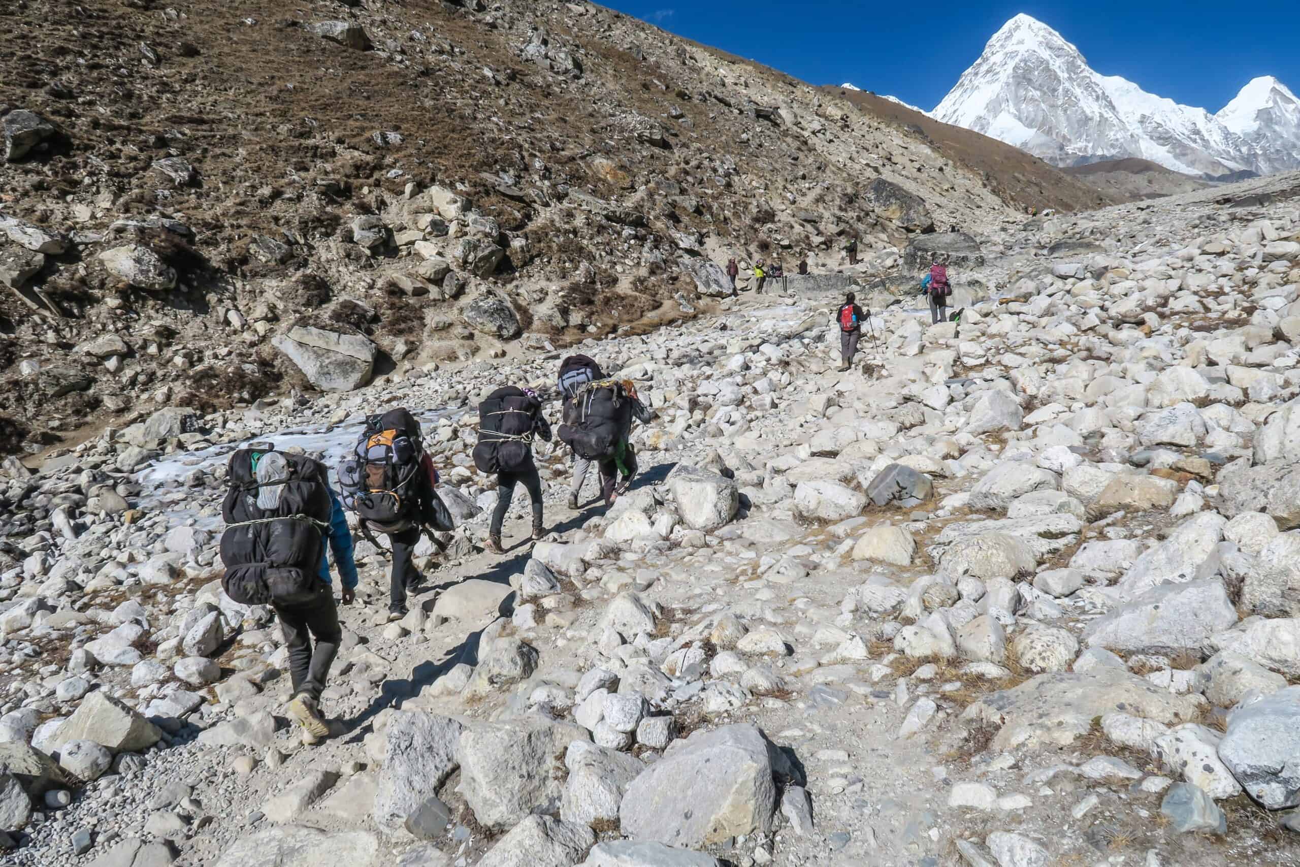 Climbing party of seven individuals traversing rocky path with large snow capped mountains in the distance