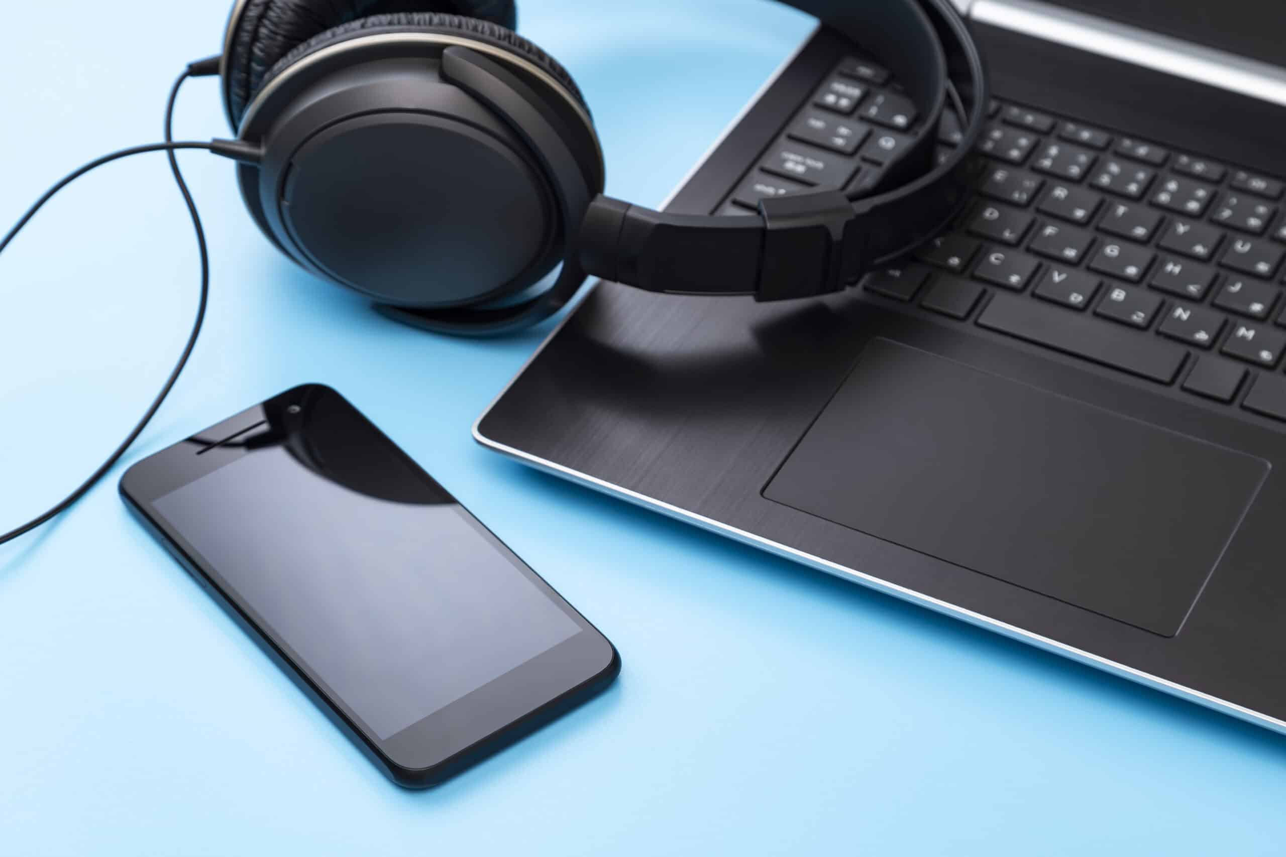 Close-up of a smartphone, over-ear headphones, and a laptop on a bright blue background to represent a screen reader