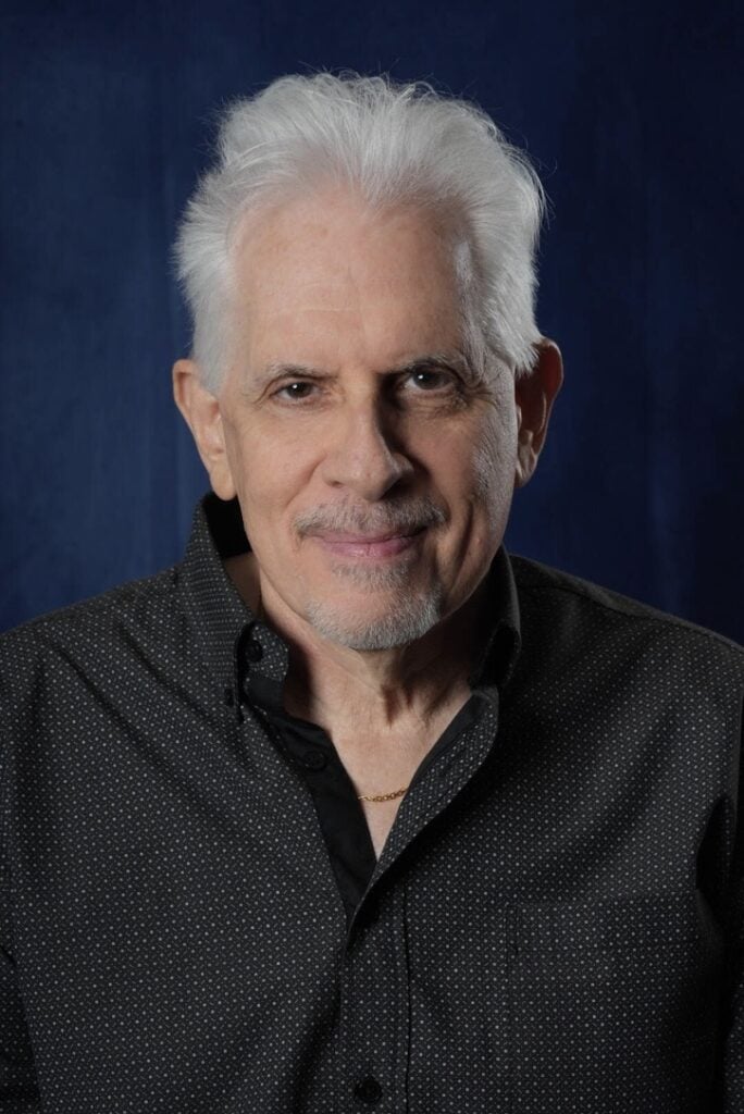 Steve smiling and posing for the camera while wearing a black and white button-up.