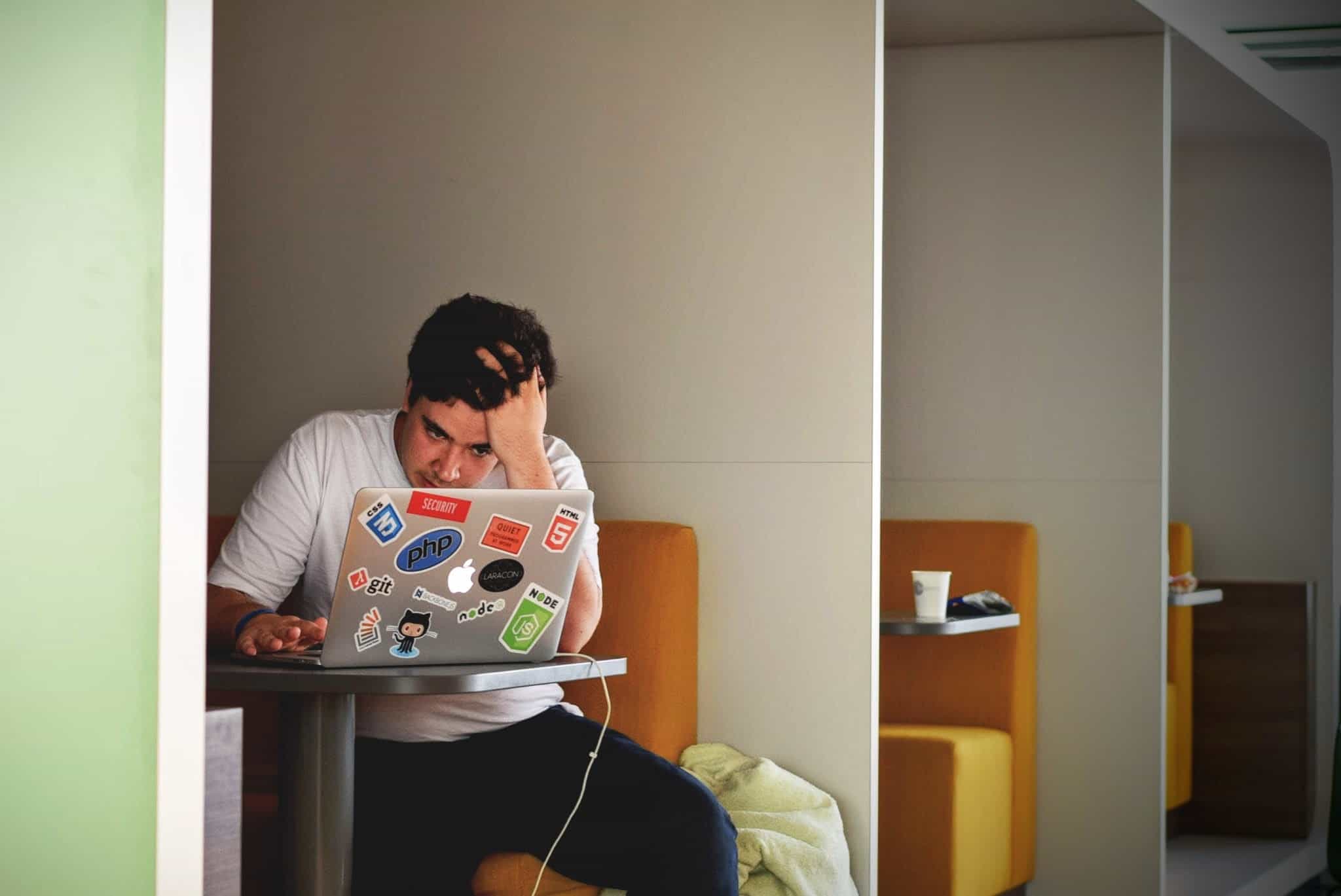 Solo individual in white t-shirt, working alone with hand on head staring at screen intently
