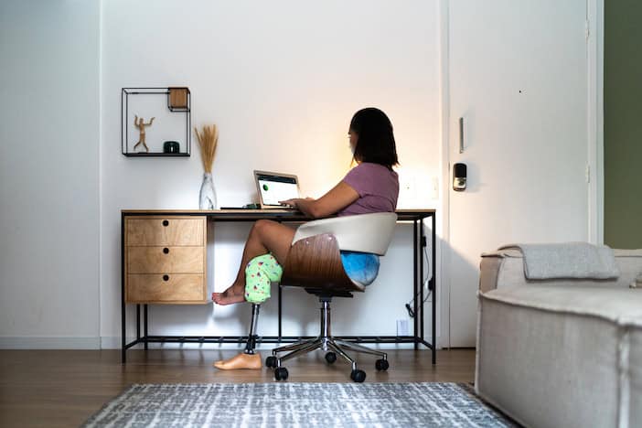 User with a prosthetic right leg using a laptop at a desk at home