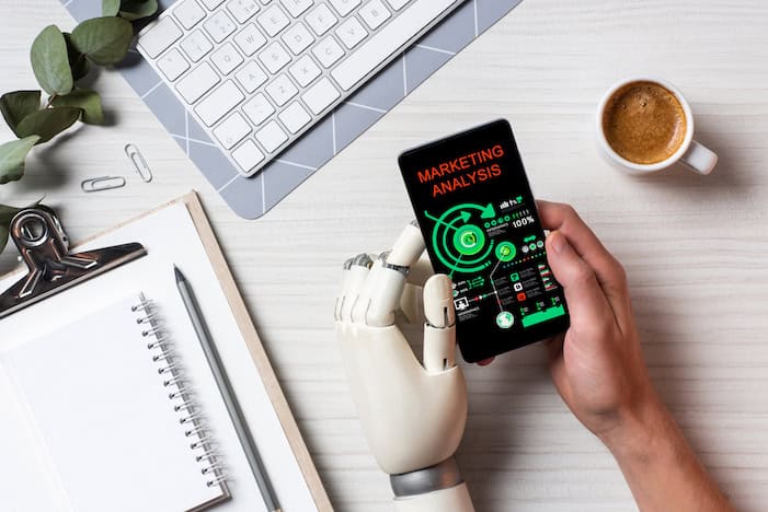 Professional with prosthetic left hand using smartphone with marketing analysis on screen at table with coffee cup in office