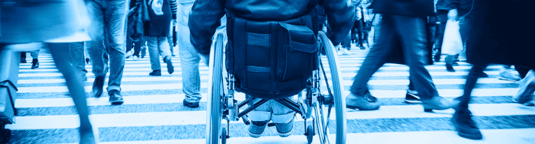 ground level view of a wheelchair user crossing a busy crosswalk filled with others
