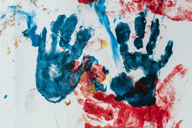 Blue handprints on a finger painted multicolored canvas