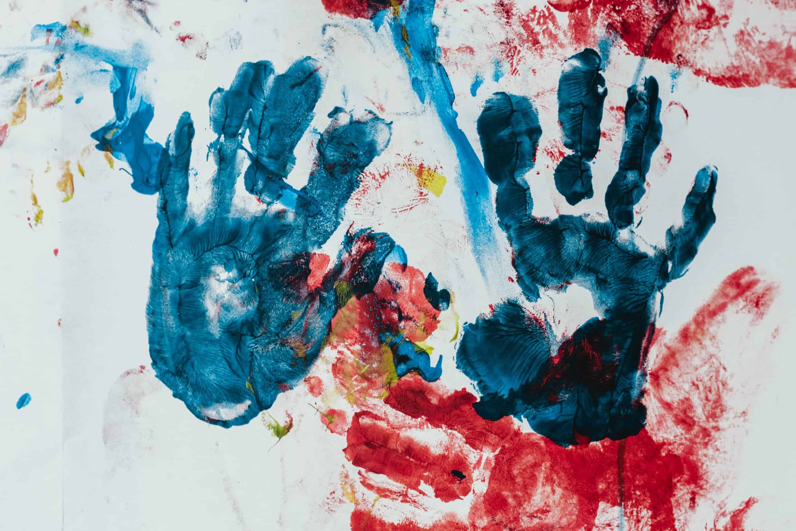 Blue handprints on a finger painted multicolored canvas