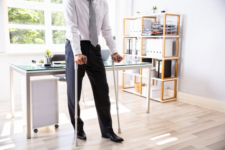 Man with crutches standing in front of desk.