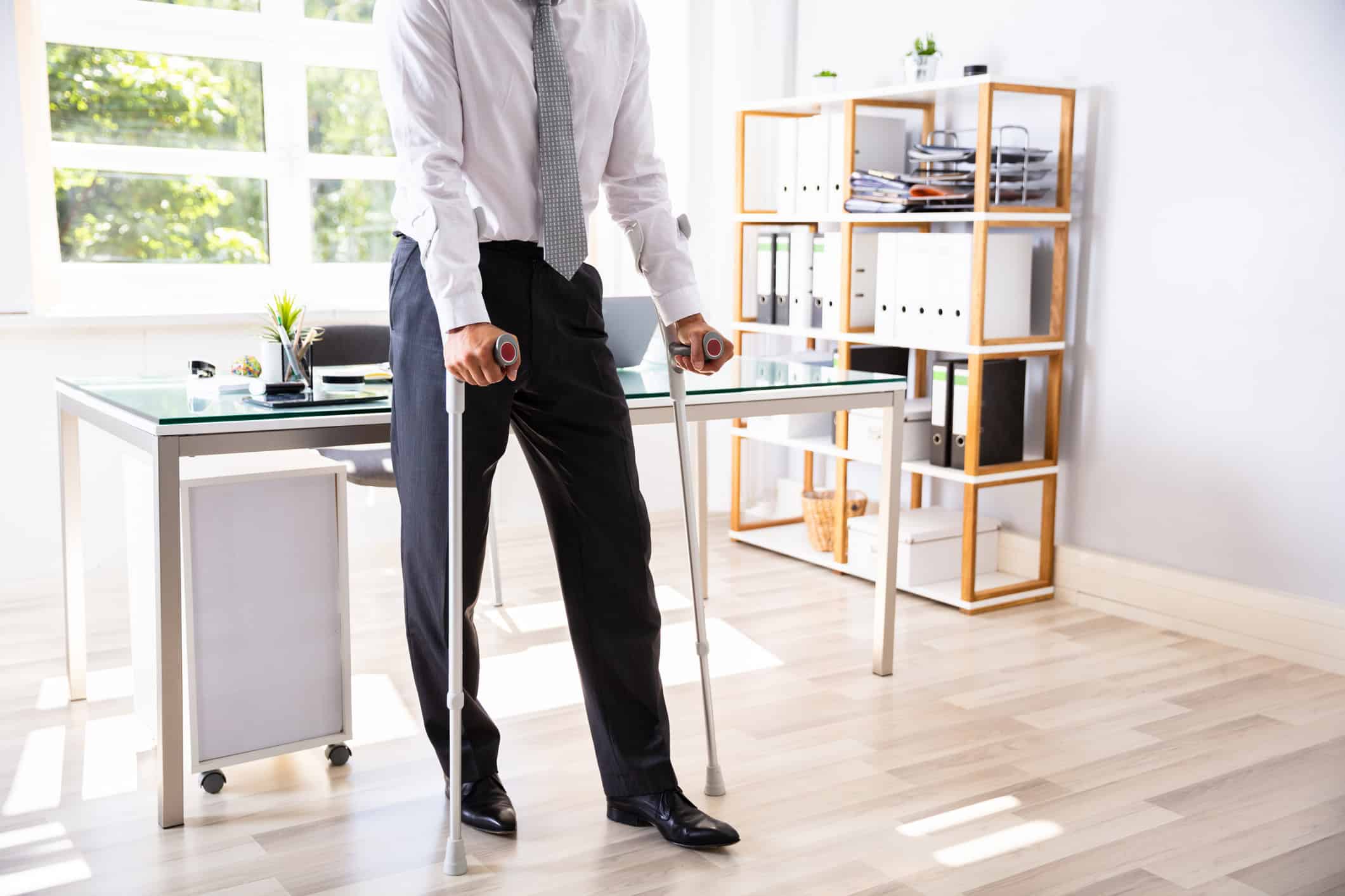 Man with crutches standing in front of desk.