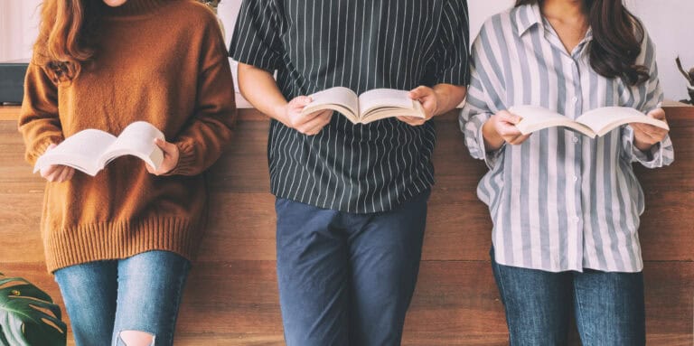 Three young people standing and reading books together.