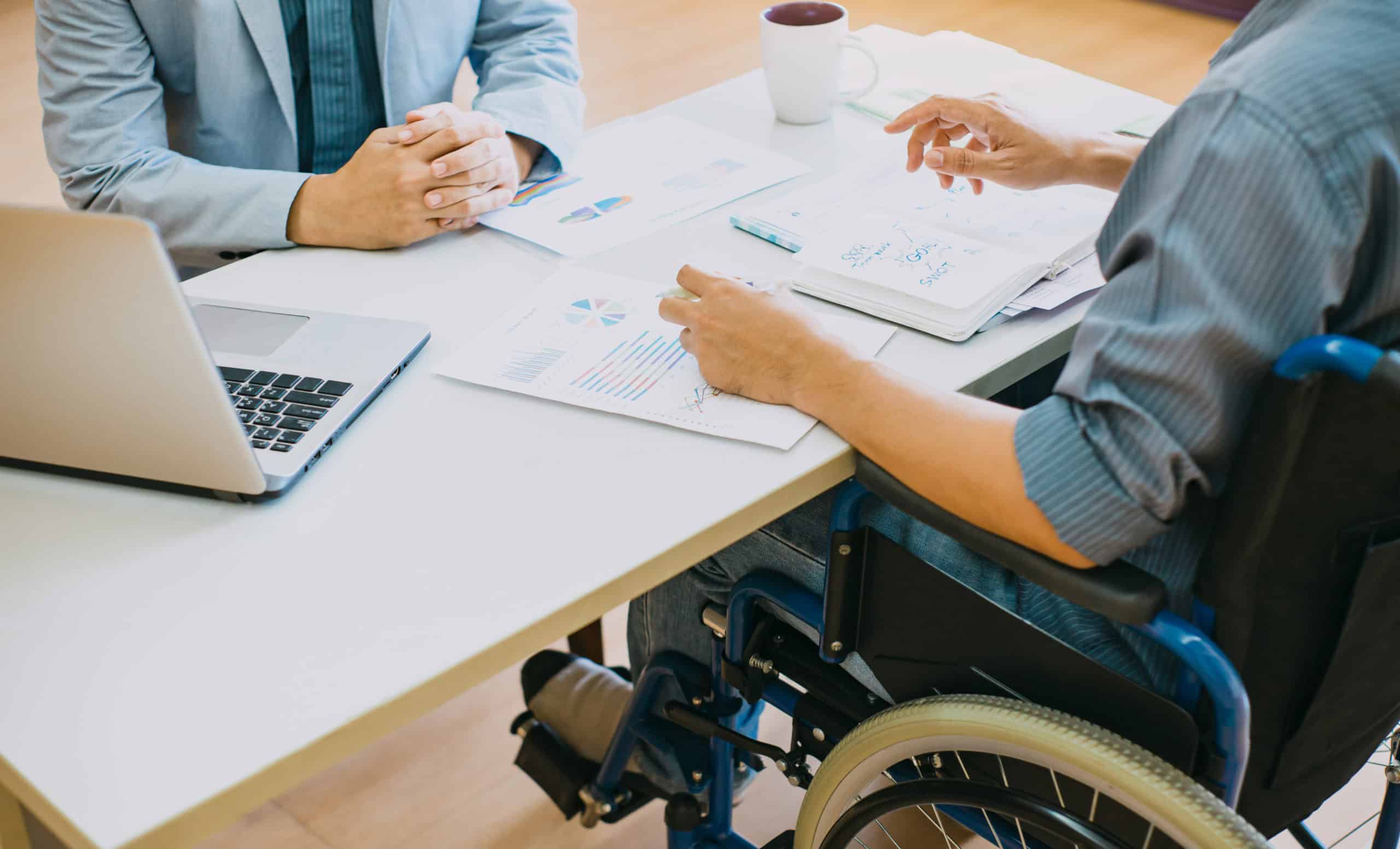 Man using wheelchair meets with someone behind a desk in an office environment.