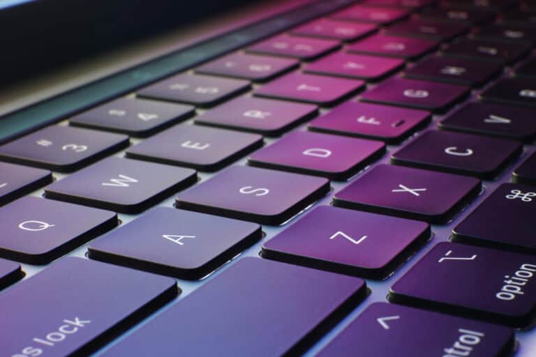 A close up of a laptop keyboard with the pink and green colors from the screen reflecting off of the keys.