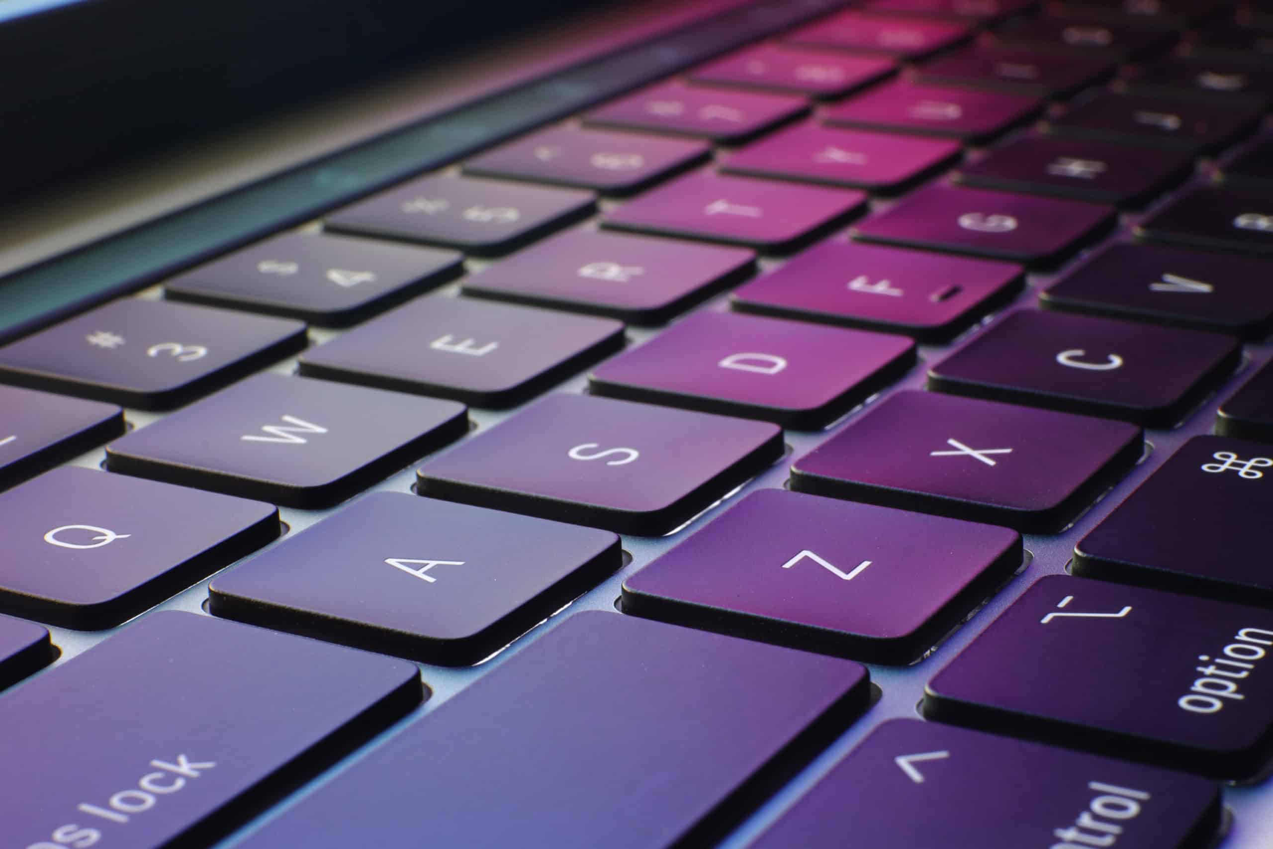 A close up of a laptop keyboard with the pink and green colors from the screen reflecting off of the keys.
