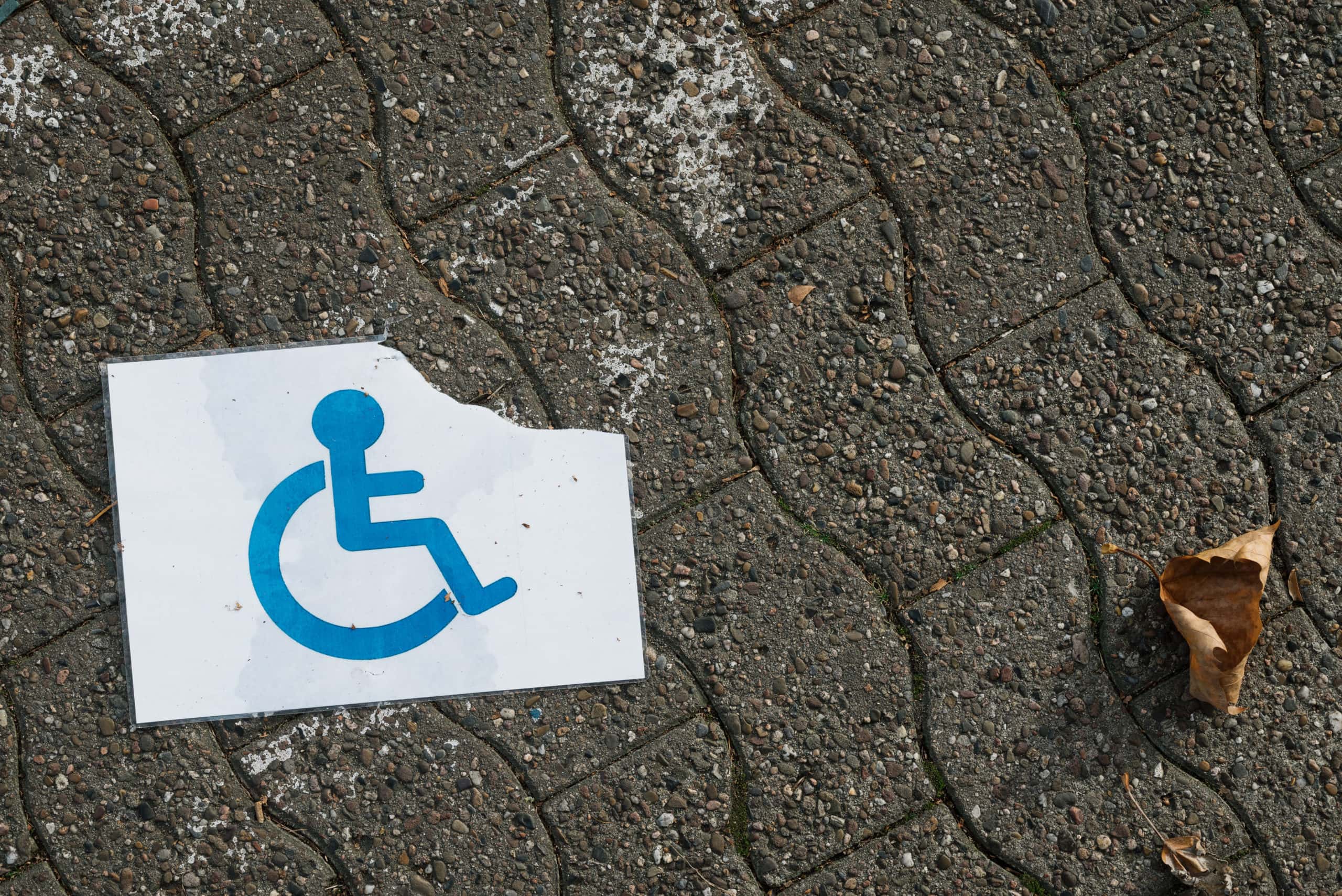 A torn and wet disabled person sign on the ground.