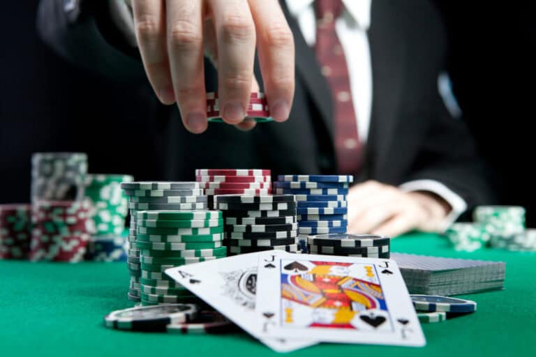 A man in a suit reaches for poker chips over a set of cards.
