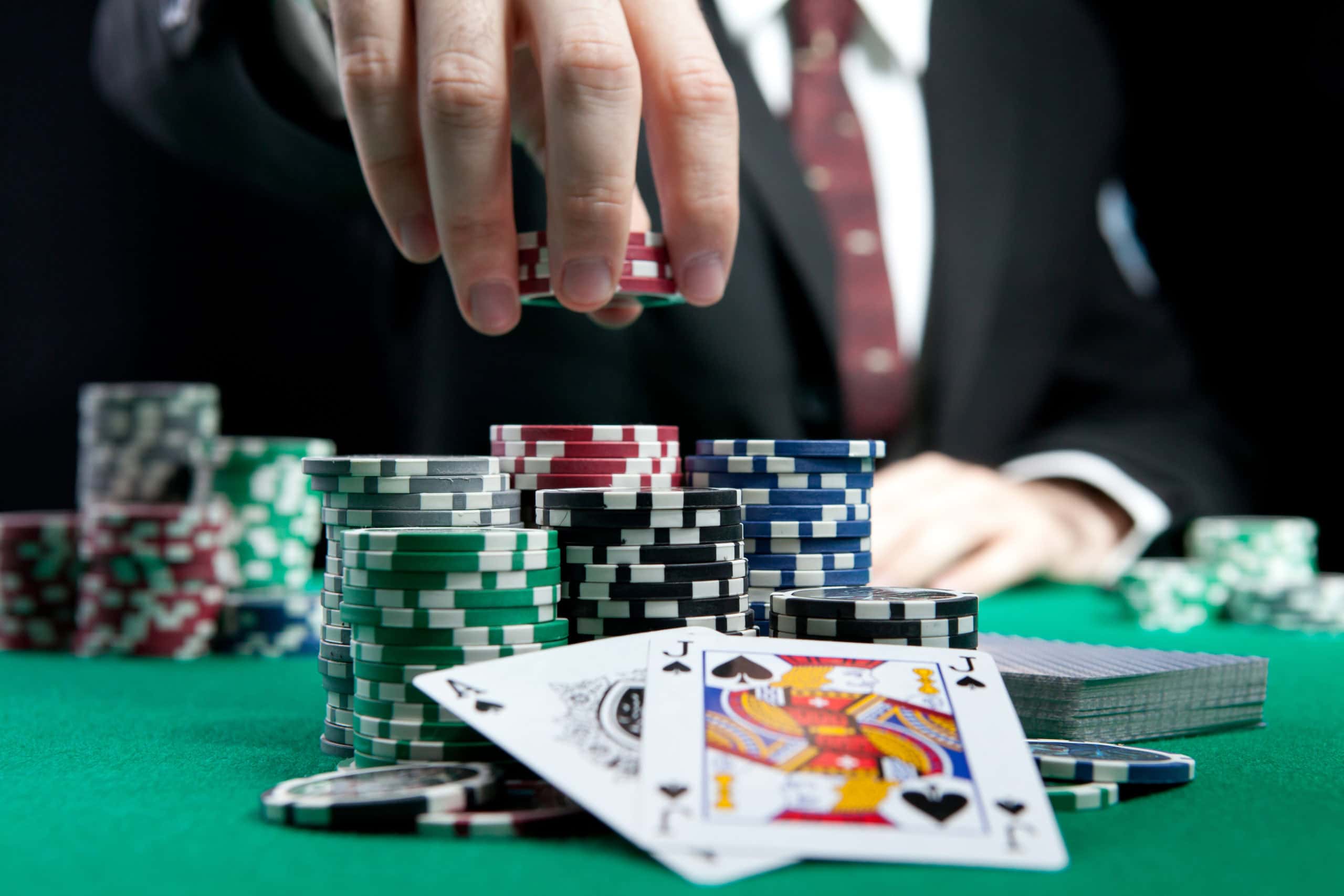 A man in a suit reaches for poker chips over a set of cards.