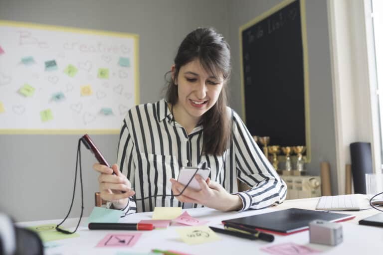 Designer with hearing aid seated at post-it strewn desk, using a recording pen hooked up to smart phone with tablet nearby