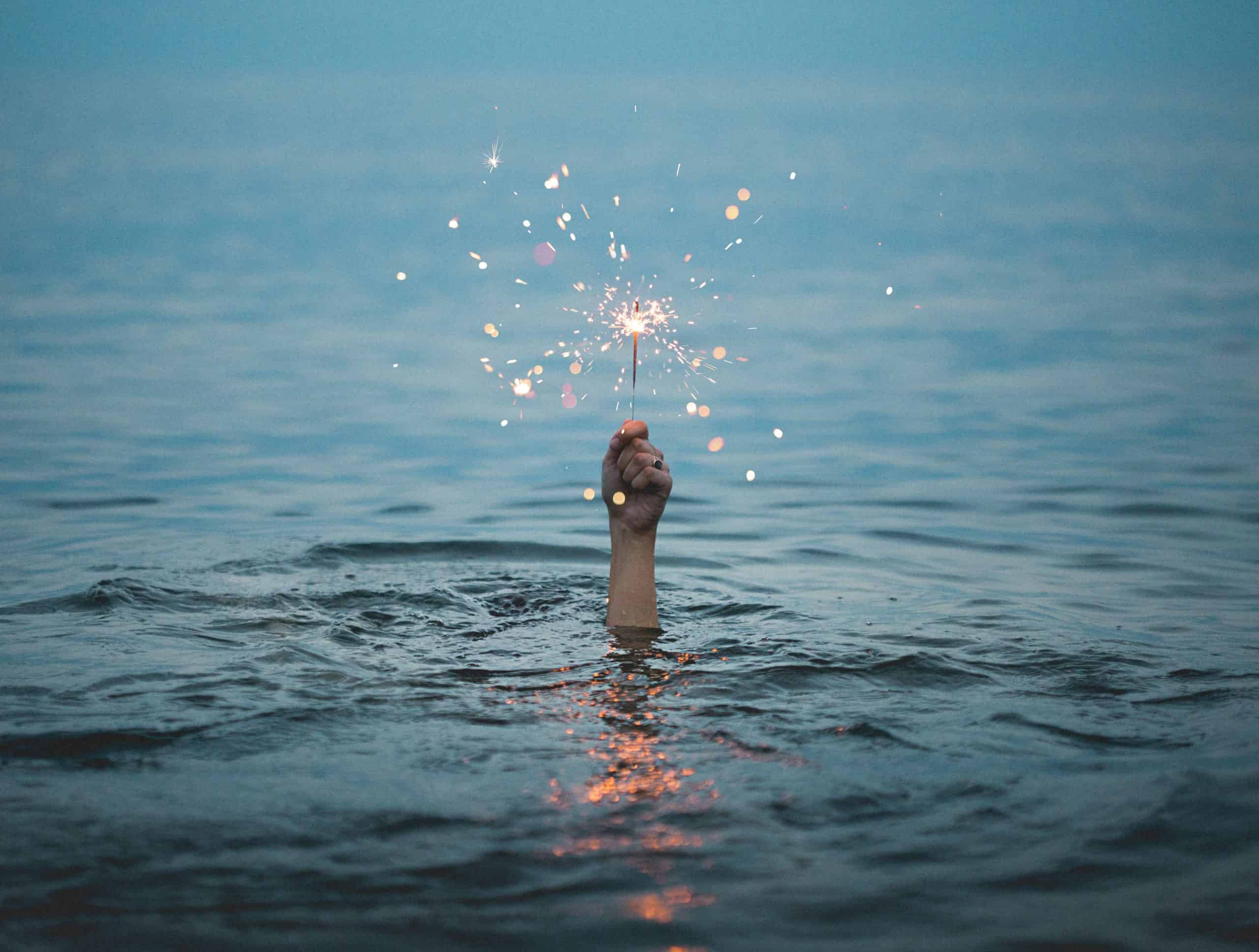 hand reaching out of the water holding a sparkler